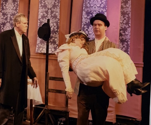 Actor carrying a woman in Victorian dress across the stage