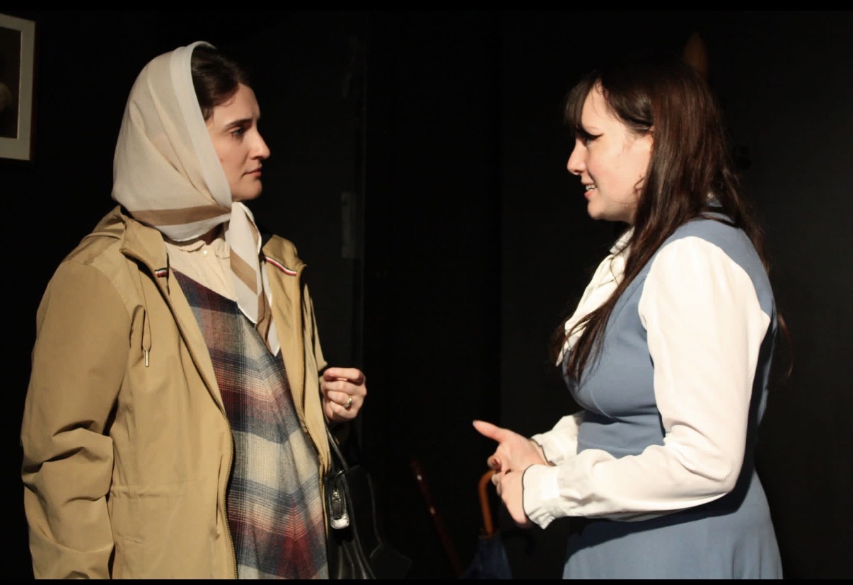Two characters facing each other mid-argument in a dim interior scene