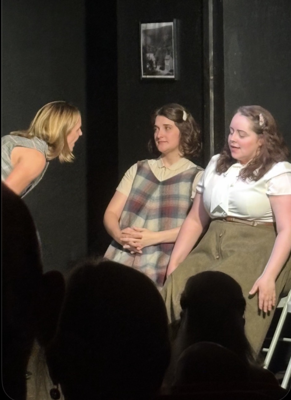 Three women seated together as a fourth leans in during a tense exchange
