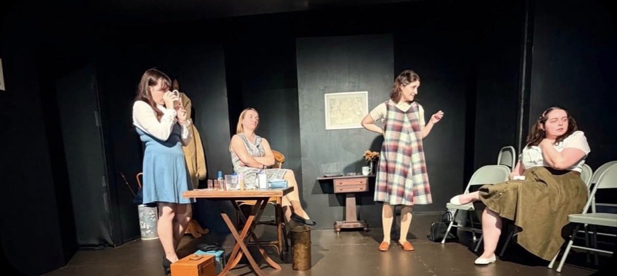 Five-woman ensemble scene in a sparse backstage dressing room